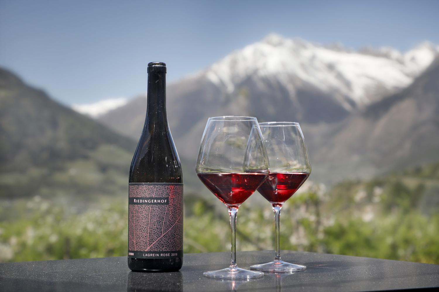 Vino del maso Riedingerhof con calici e montagne sullo sfondo 